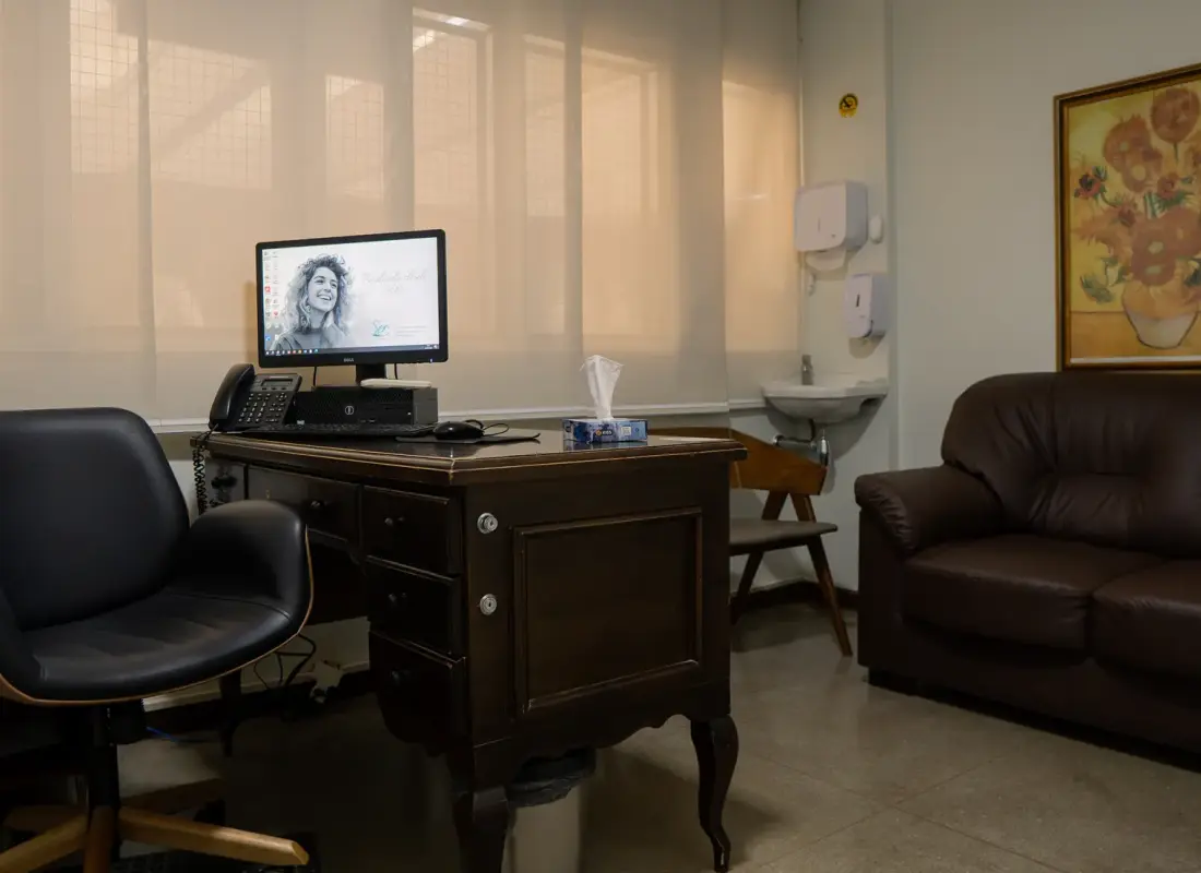 Consultório com mesa de atendimento, poltrona e sofá para acompanhante