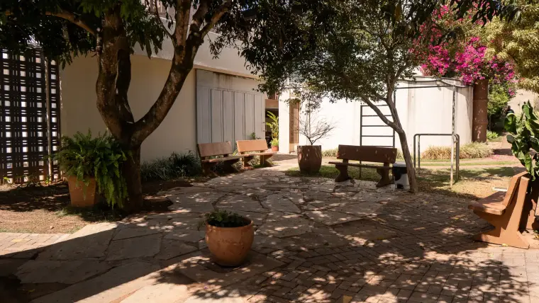 Jardim interno com bancos de madeira à sombra das árvores
