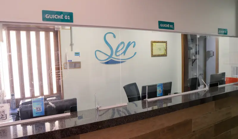 Guichês de atendimento da recepção com a marca Ser na parede