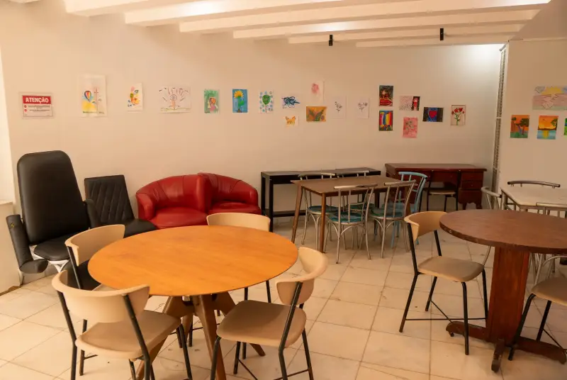 Sala de atividades terapêuticas com mesas redondas e trabalhos dos pacientes na parede