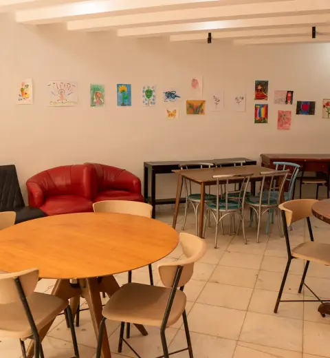 Sala de atividades terapêuticas com mesas redondas e trabalhos dos pacientes na parede