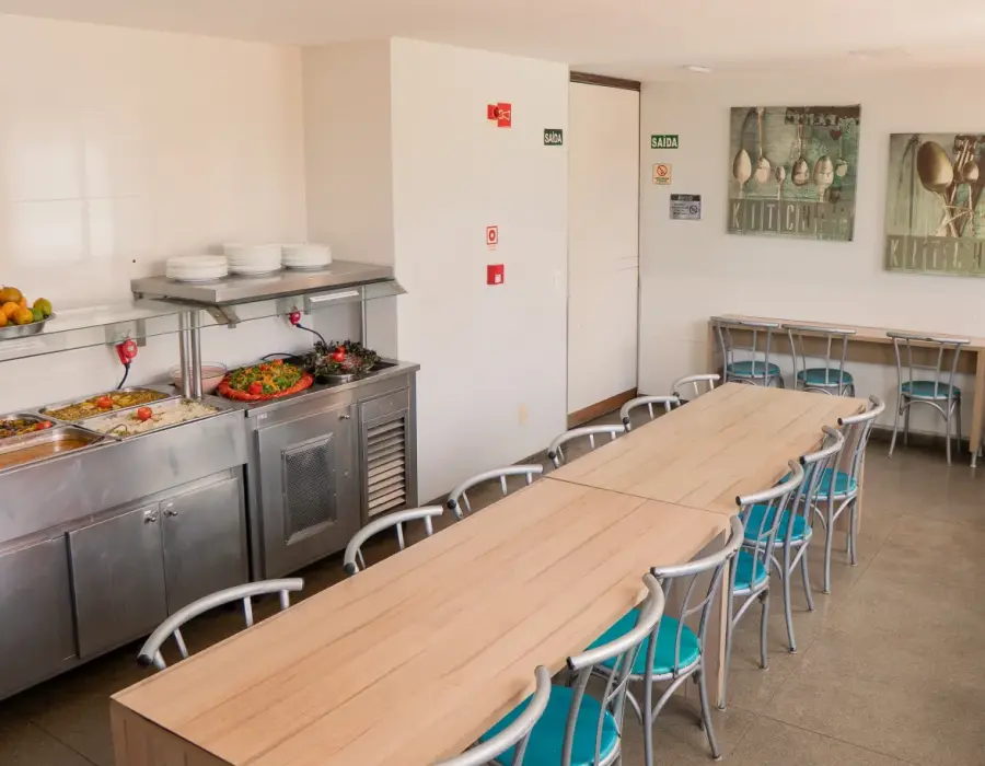 Refeitório com mesa comunitária e balcão de refeições.